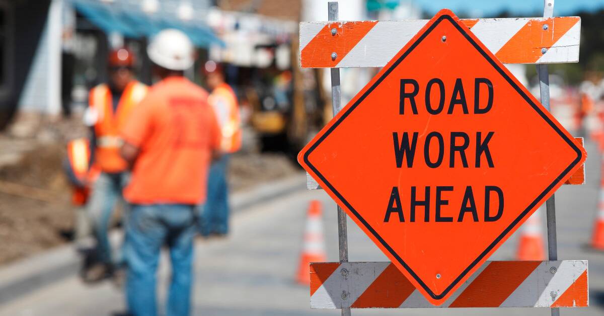 A 'road work ahead' sign with workers visible in the background.