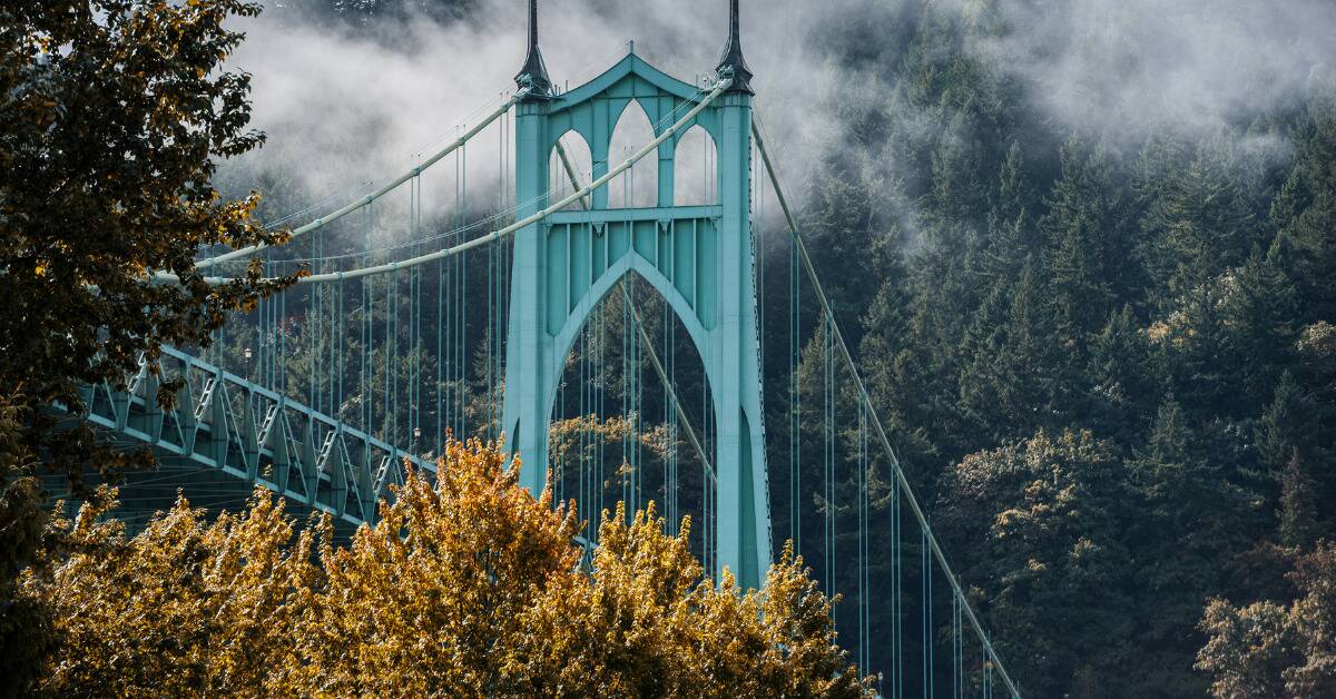 A photo of a bright blue bridge in Portland in front of a forest backdrop.