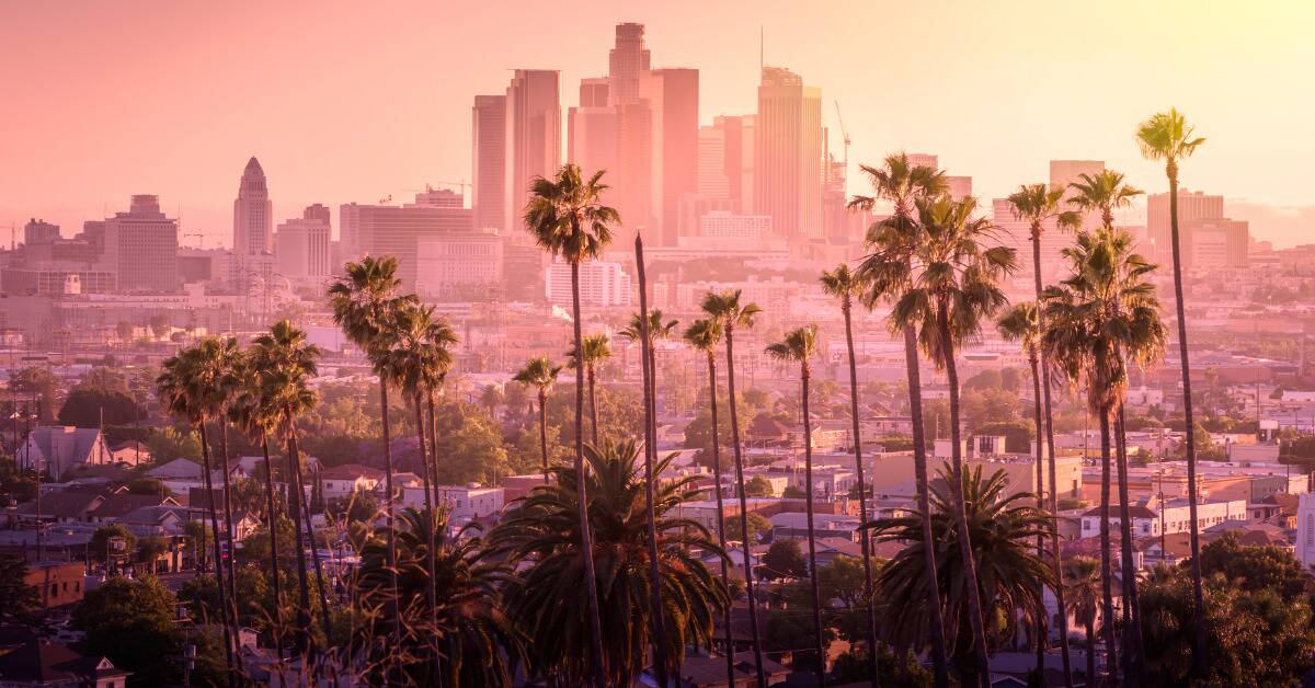 The Los Angeles cityscape, tinted pink, manyt palm trees in the foreground.