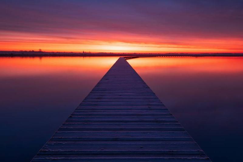 Sunset on a boardwalk into a lake.
