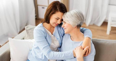 A mother and her adult daughter sitting on a couch, hugging close and looking into each other's eyes.
