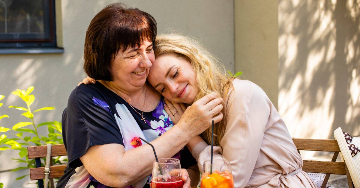 A woman hugging her adult daughter, who's leaning her head against her mother's shoulder.