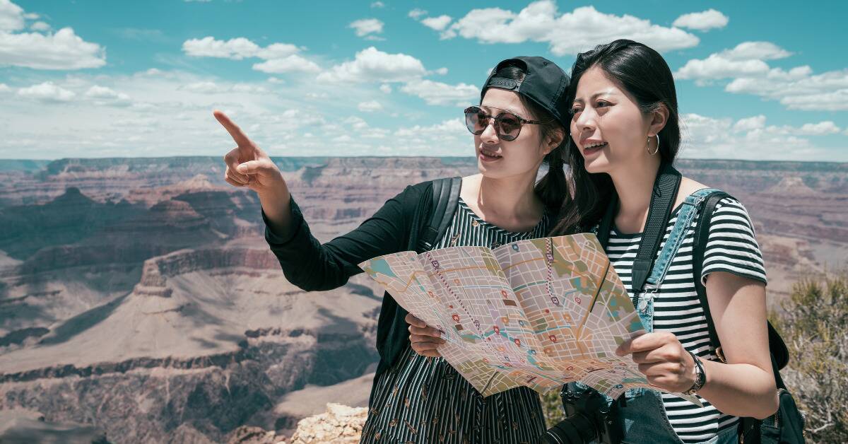 Two women standing by a canyon, holding an open map and pointing at where they're walking next.