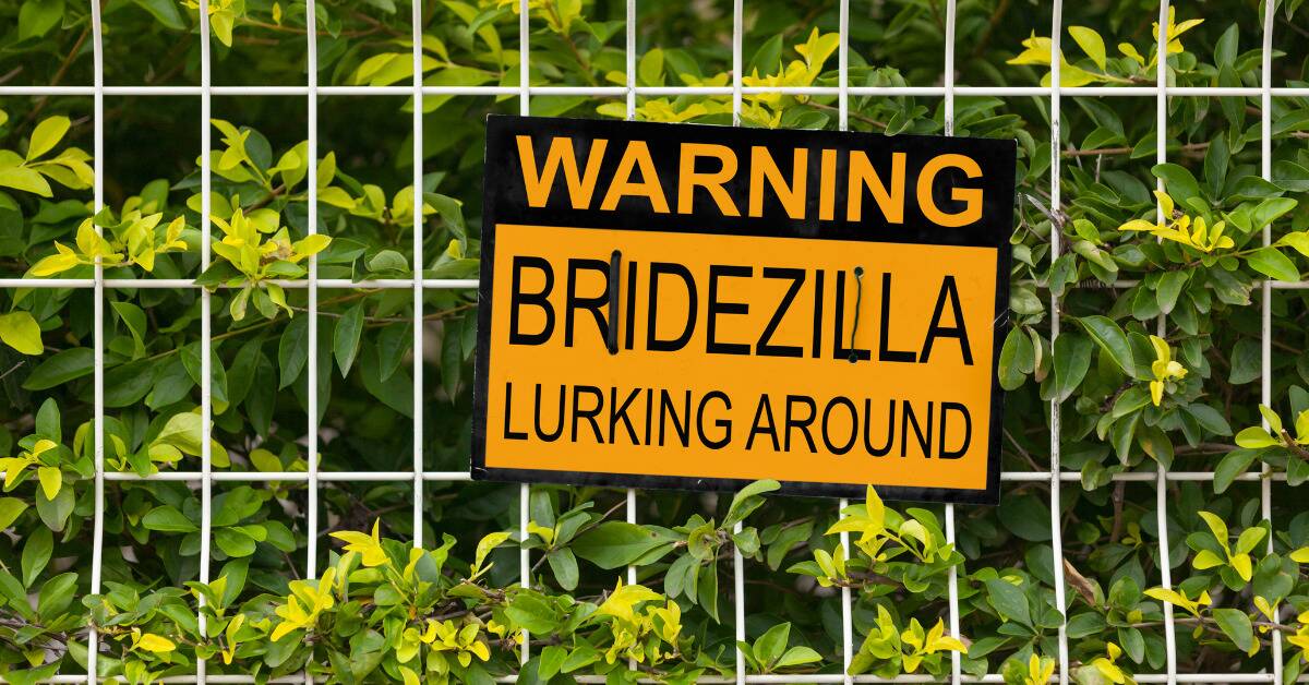 A yellow warning sign on a fence in front of a hedge that reads, 