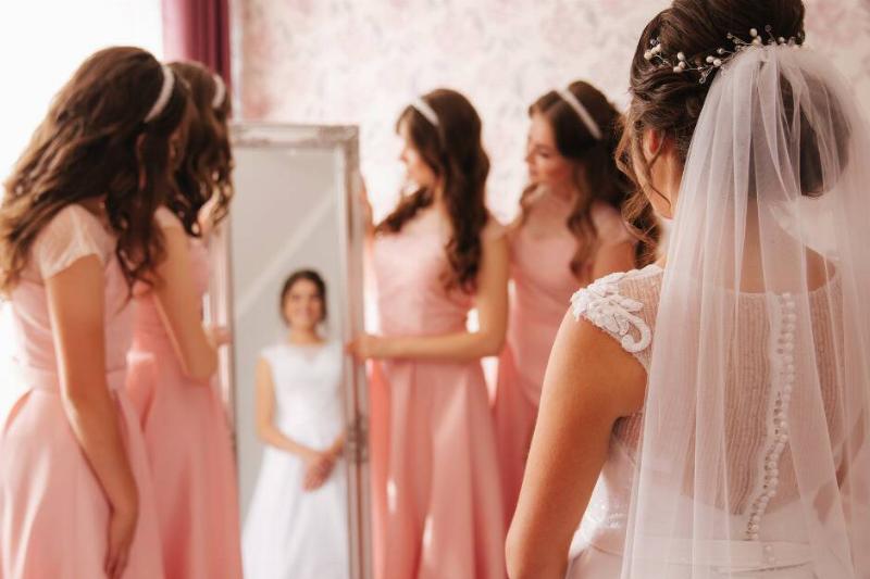 A bride seeing herself in her dress in the mirror, surrounded by her bridesmaids.
