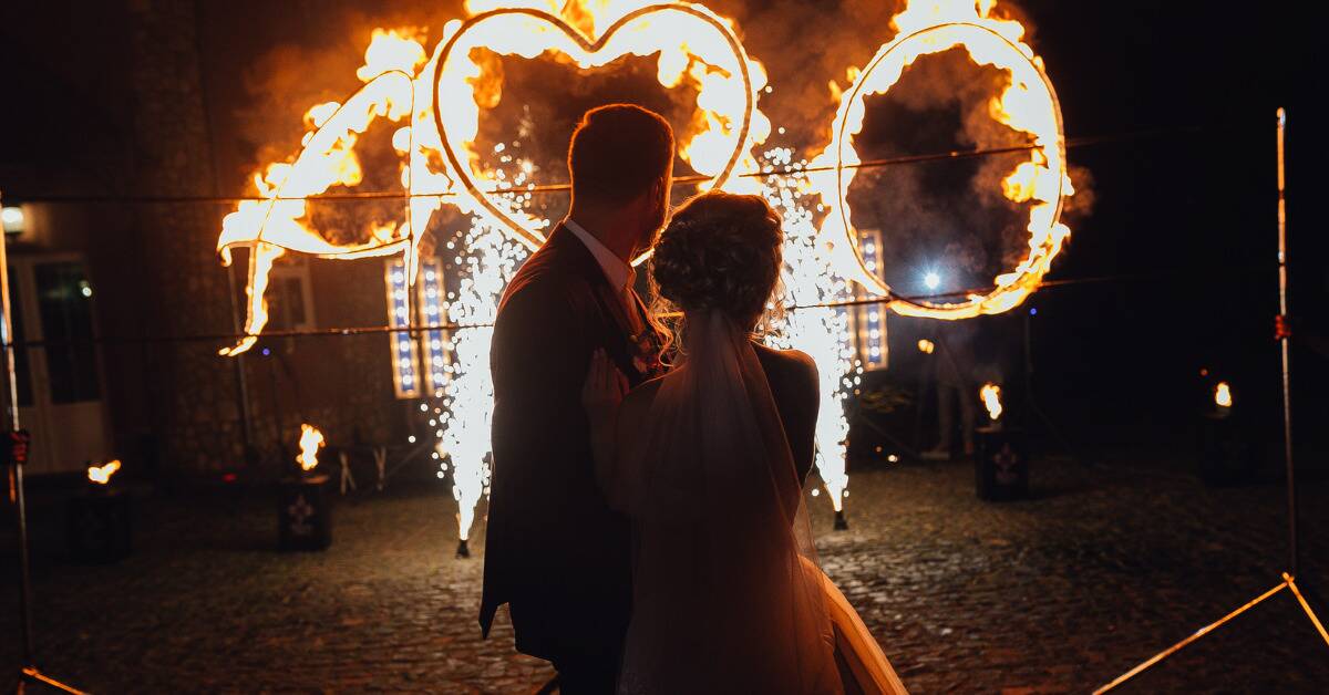 A married couple standing in front of and watching a large heart on fire.