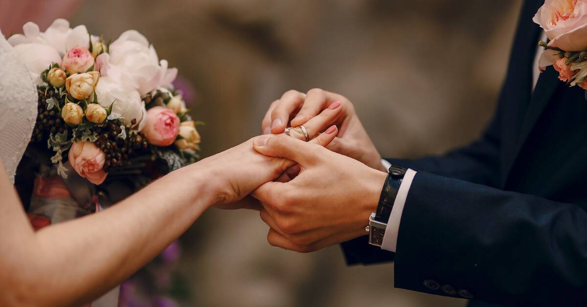 A close shot of a man putting the wedding band on his bride's finger.
