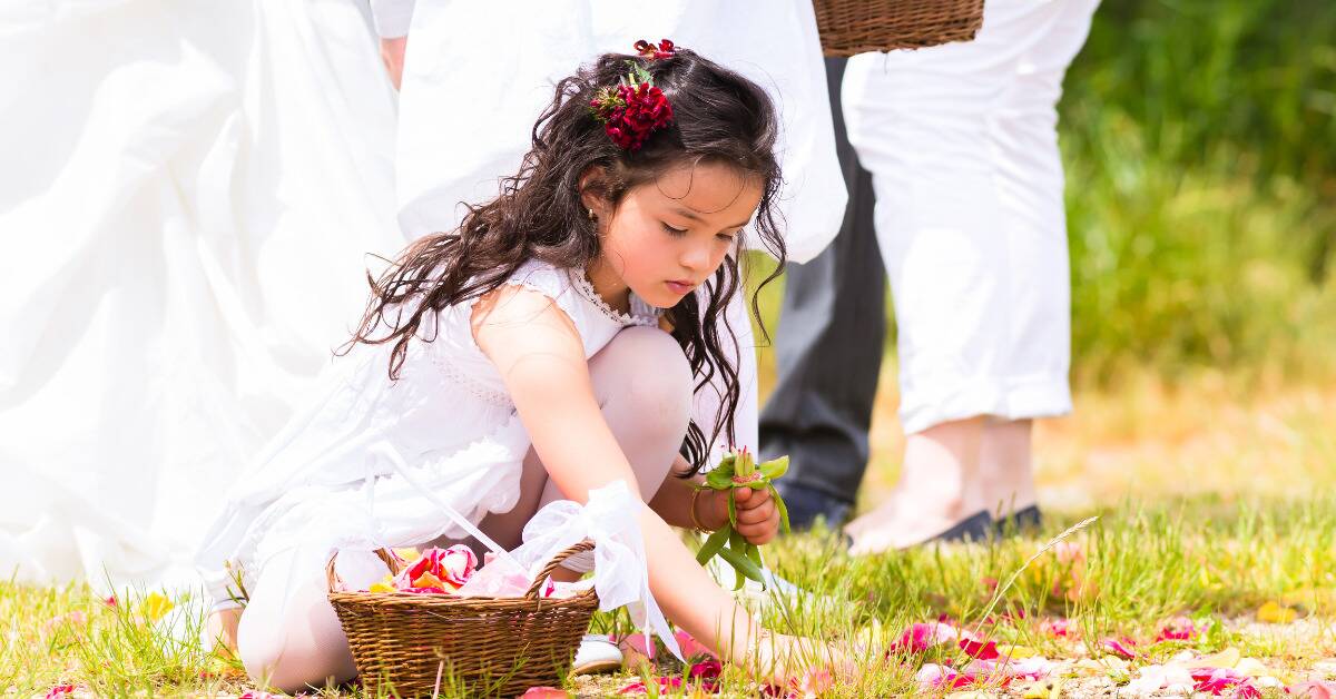 A flower girl crouched on the ground spreading petals.