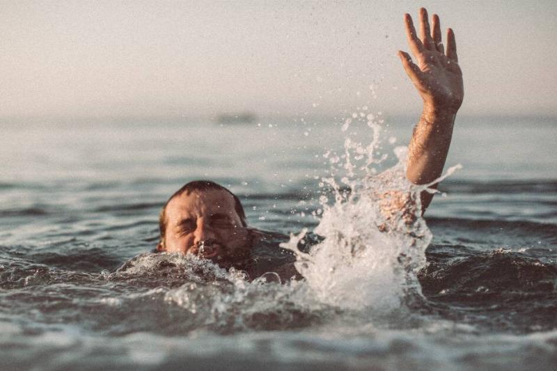 A man drowning, one hand reaching above water as he tries to push his head above the surface.