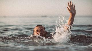 A man drowning, one hand reaching above water as he tries to push his head above the surface.