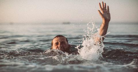 A man drowning, one hand reaching above water as he tries to push his head above the surface.