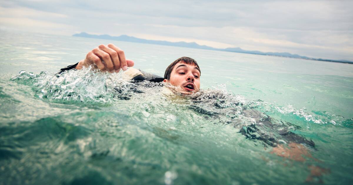 A man swimming chaotically with his head just above water.
