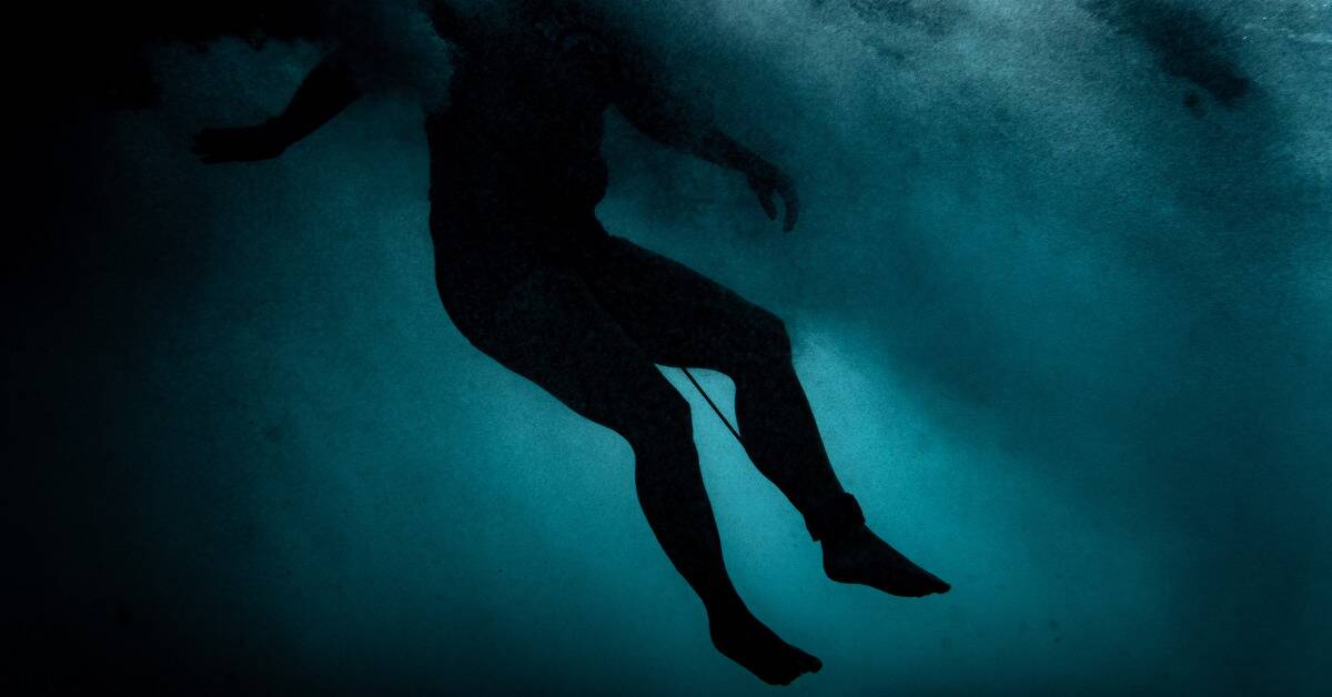 A silhouette of someone underwater, a rope around their ankle.