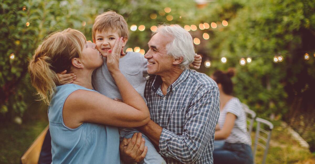 Two grandparents holding their young grandson, the grandmother kissing one of his cheeks.