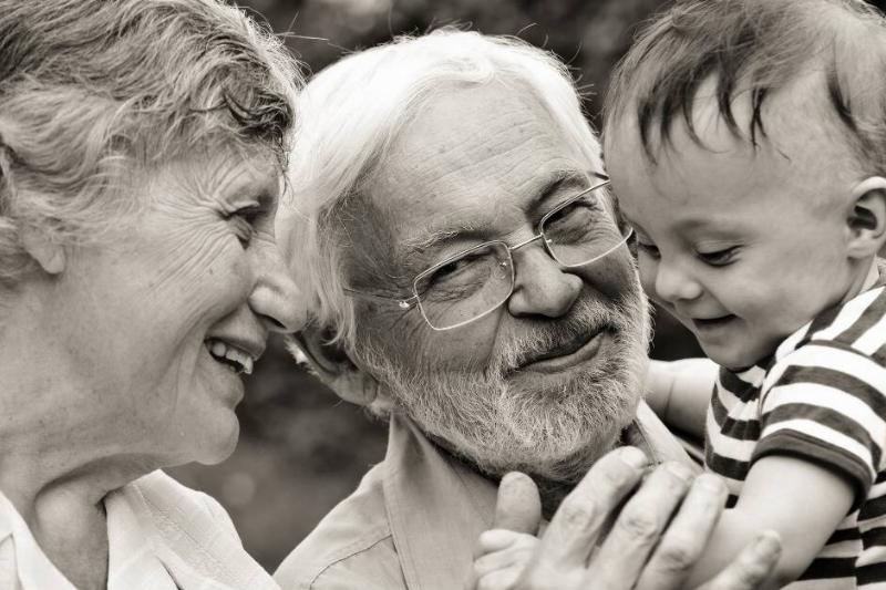 A greyscale image of two grandparents holding their very young grandson, all smiling.