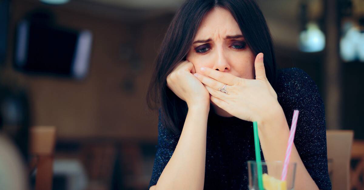 A woman sat at a table, looking uncomfortable as she covers he mouth for a hiccup.