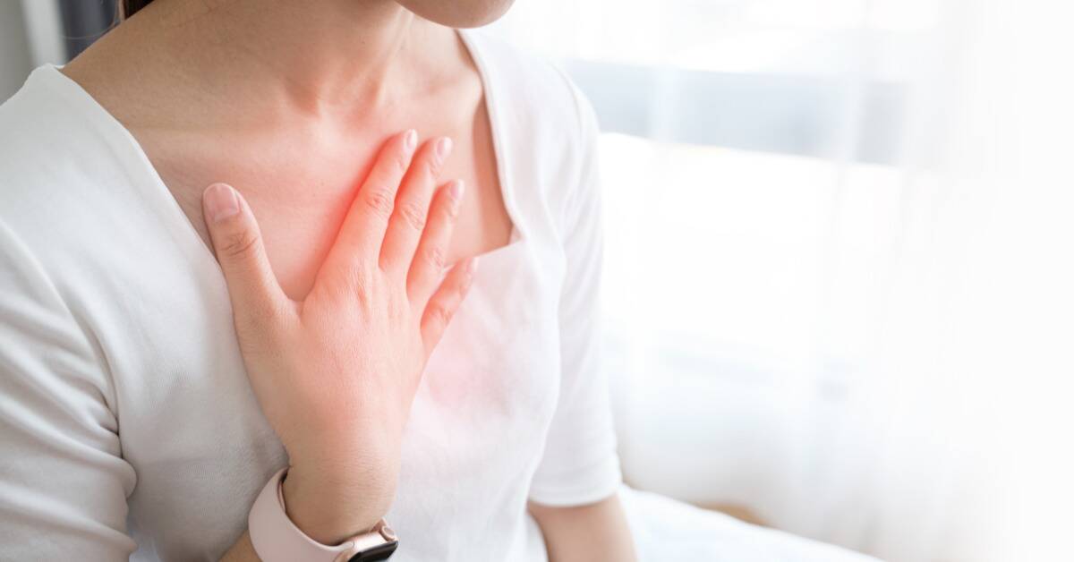 A woman with her hand on her chest, a faint red glow emanating from it as if it's a source of pain.