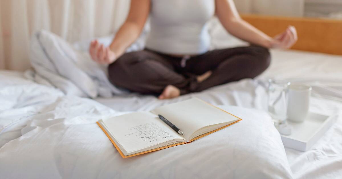 A journal open on a bed, the owner meditating in the background.