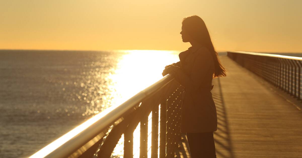 A woman leaning on a railing on a boardwalk, overlooking the water.