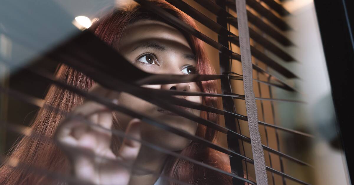 A woman pulling down some blinds so she can peer through them to the world outside.