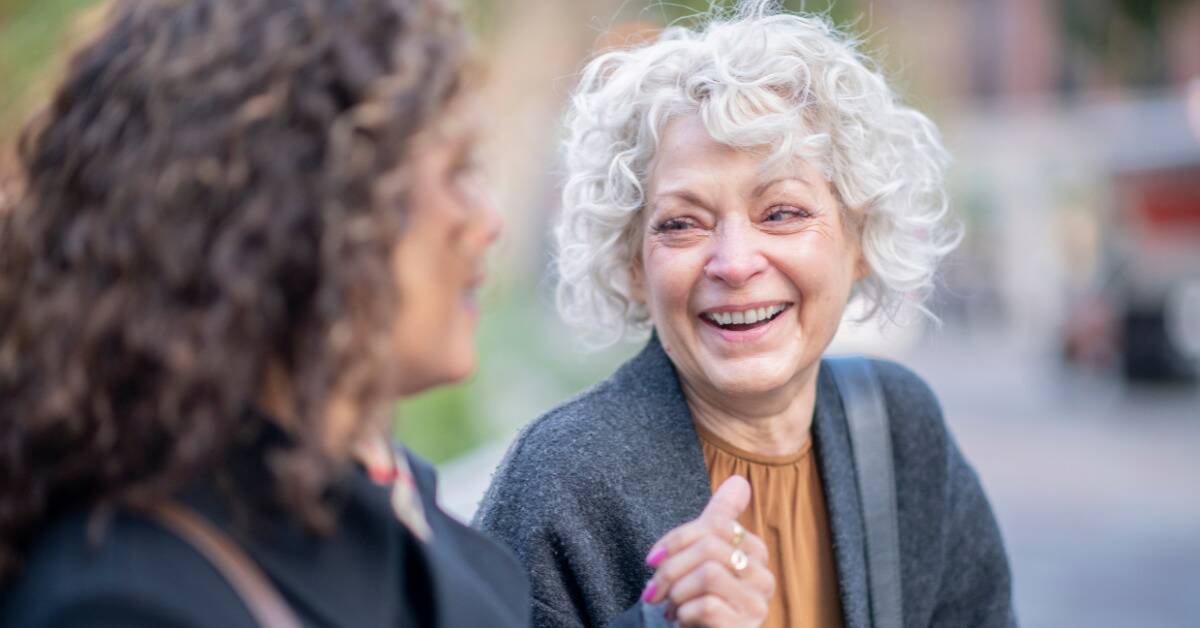 A woman smiling as she talks to a friend outside.