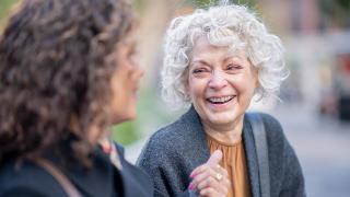 A woman smiling as she talks to a friend outside.
