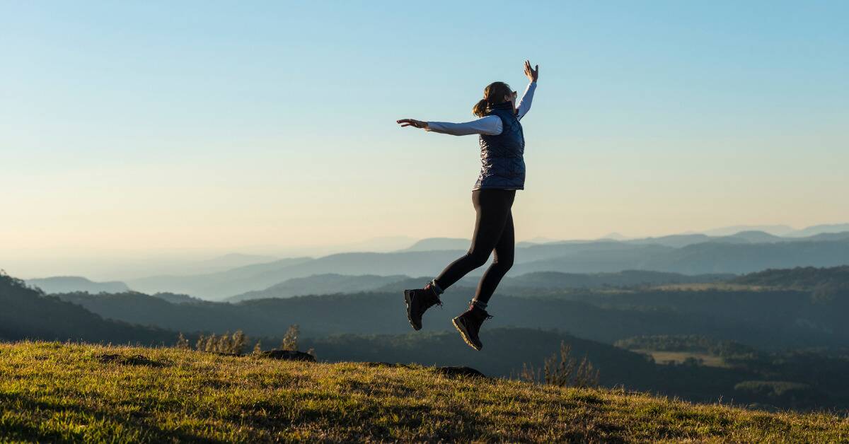 A woman jumping in the air while standing in the hillside.