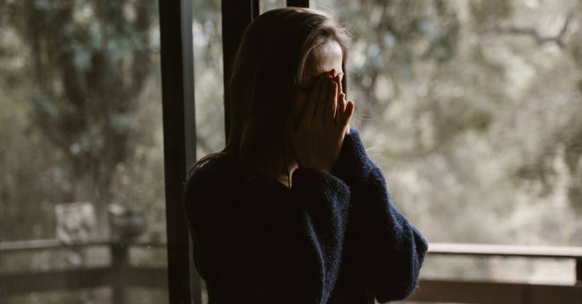 A woman in heavy shadow covering her face with both her hands.