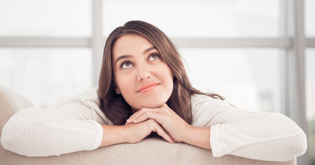 A woman leaning her chin on her folded arms, looking up as if lost in a daydream.