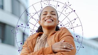 A woman standing outside, eyes closed and smiling, hugging herself. Behind her is a purple wheel graphic filled with zodiac constellations.