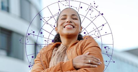 A woman standing outside, eyes closed and smiling, hugging herself. Behind her is a purple wheel graphic filled with zodiac constellations.