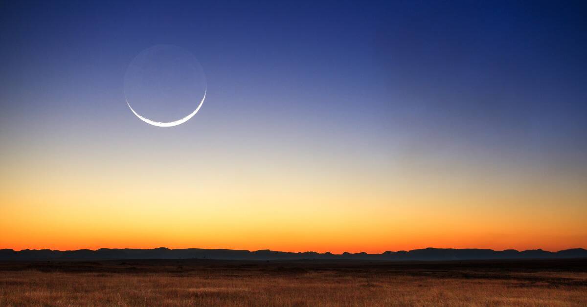 The new moon visible above a bright sun-rise horizon.