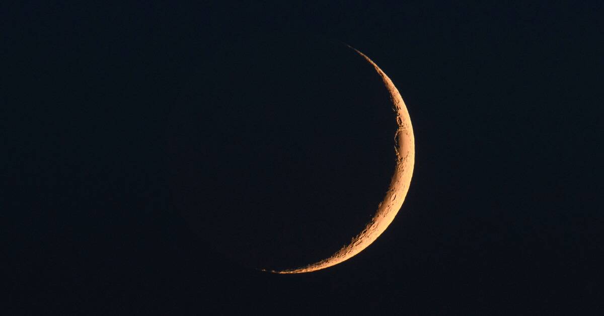 A close shot of the crescent of a new moon in a black sky.