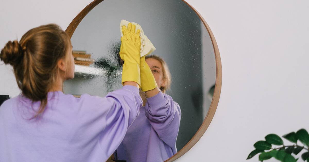 A woman cleaning and wiping down a large round mirror.