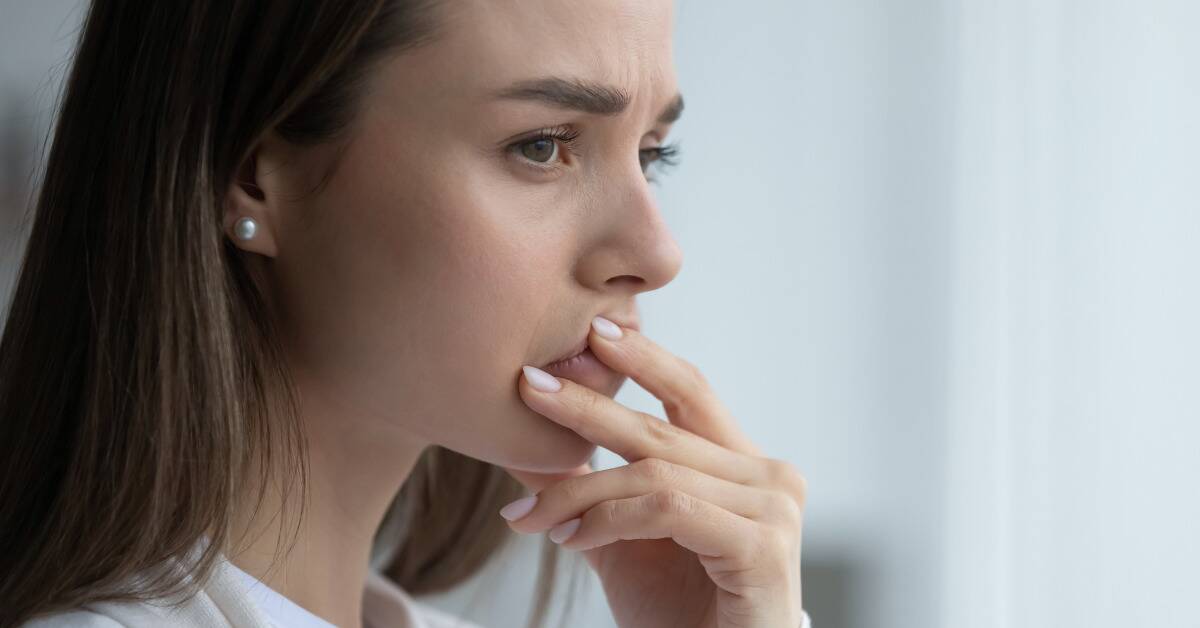 A woman with her hand to her mouth, looking thoughtful, concerned, and introspective.