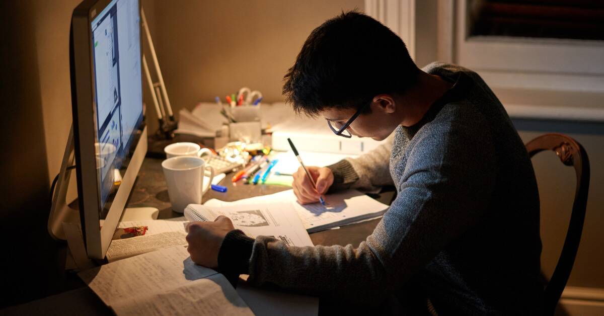 A student sitting at his desk late at night, studying intensely.