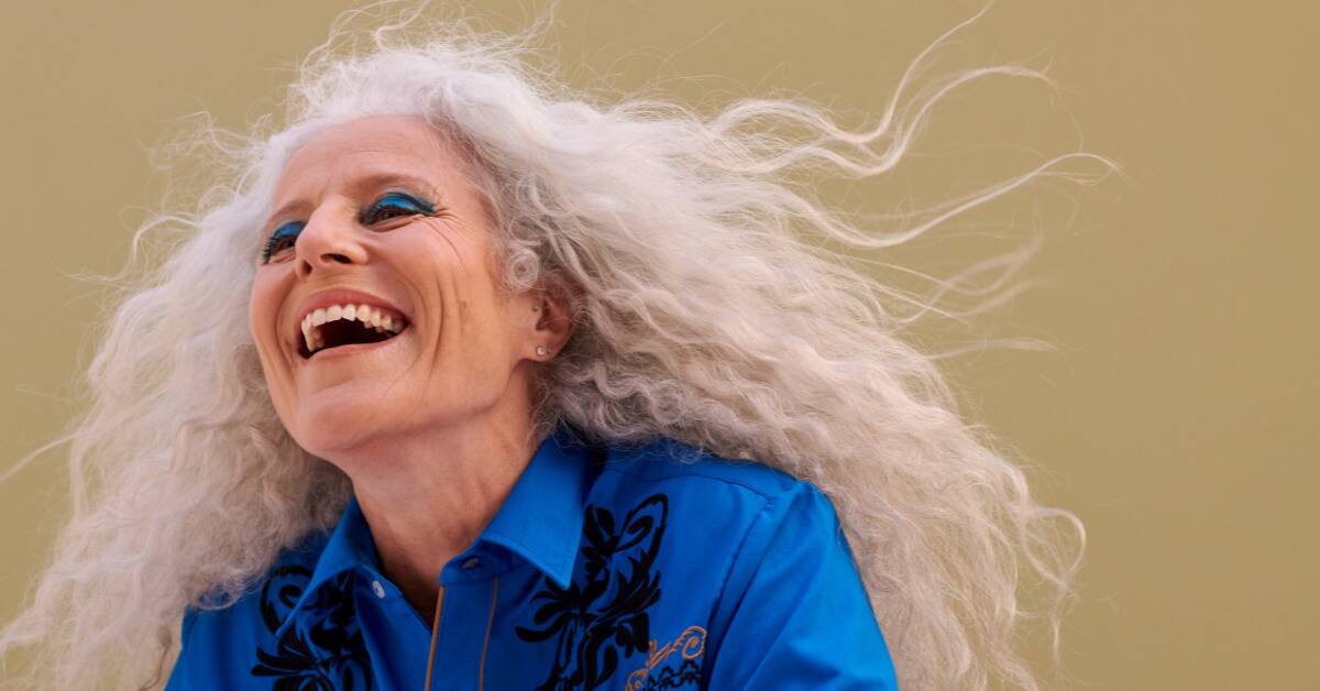 A woman in bold blue makeup smiling as her hair blows in the wind.
