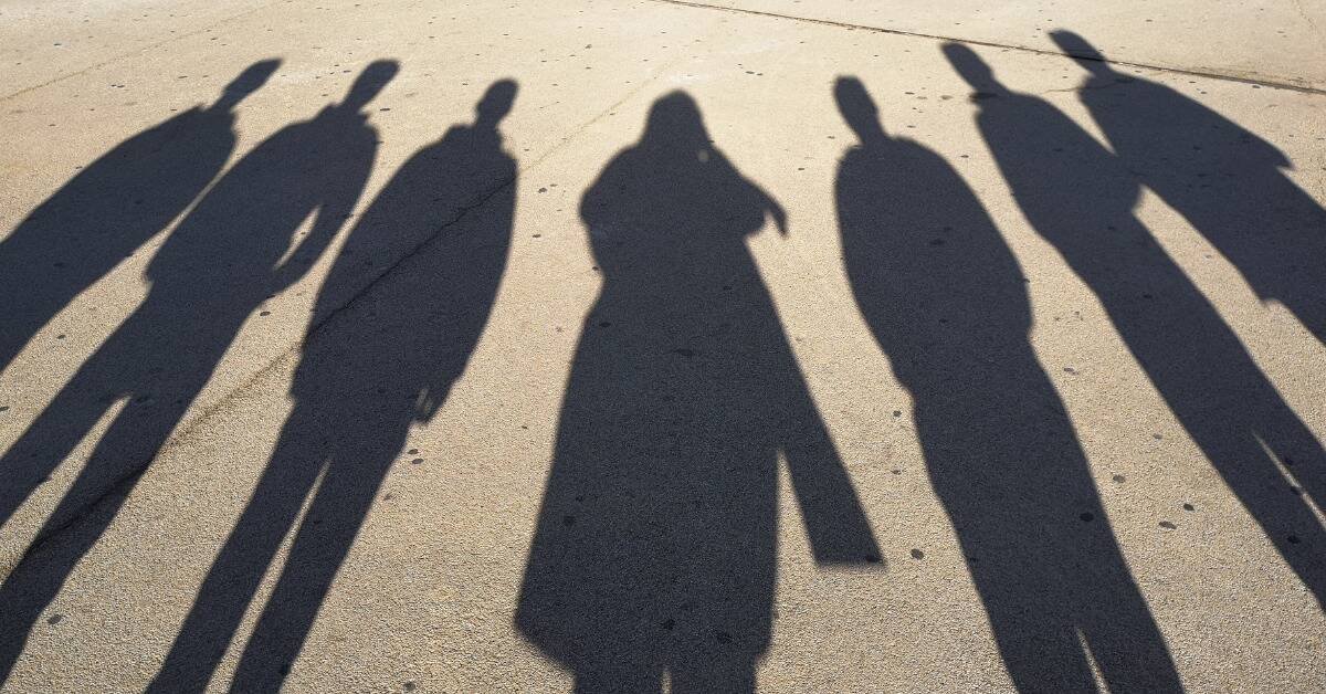 The long shadows of seven people standing next to each other outside.