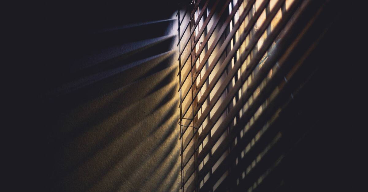 A close shot of half-closed blinds projecting shadows onto the wall.