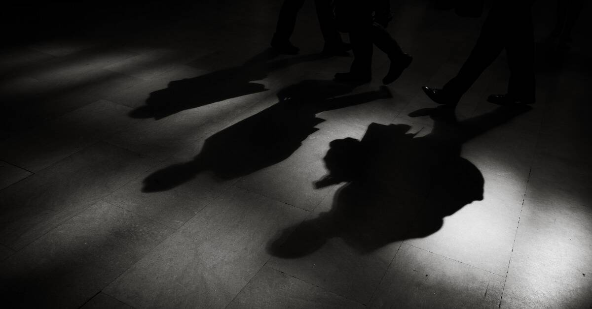 The shadows of three people walking slightly behind one another in a dark space.