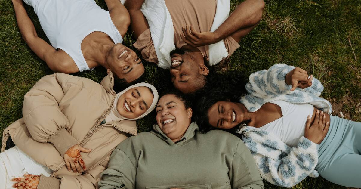 A group of friends laying in the grass together, their heads all in the center as they lay in a circle.
