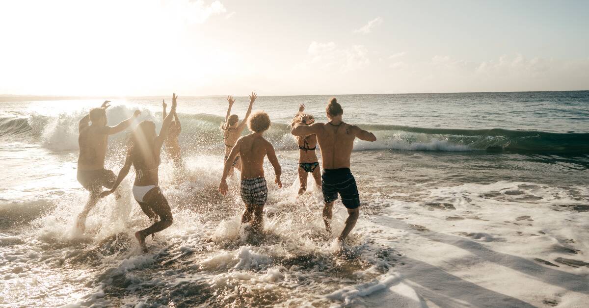 A group of friends running and jumping into the ocean off a beach.