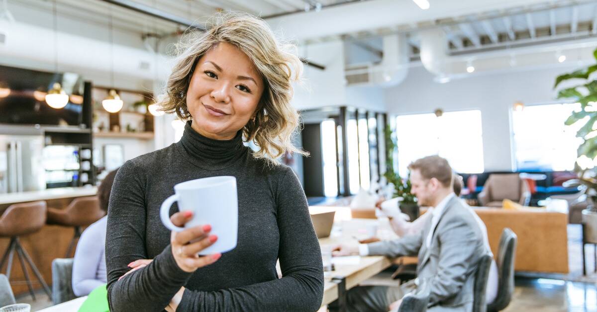 A woman at work holding a mug, smiling at the camera.