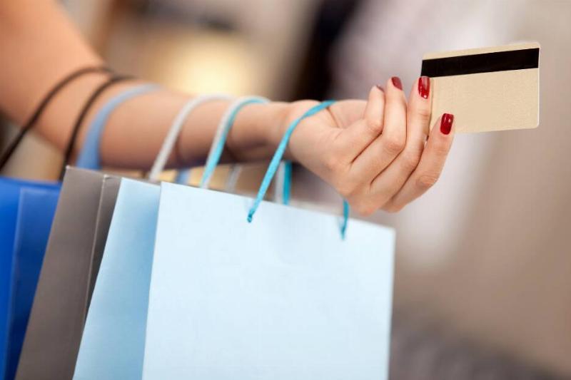 A woman with shopping bags all down her arm holding out a credit card.