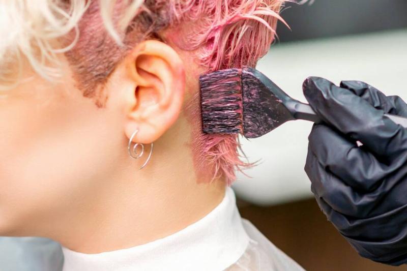A close shot of someone applying pink hair dye to someone's short bleached hair.