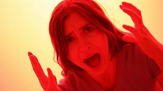 A woman shouting, hands by her head, lit in red.