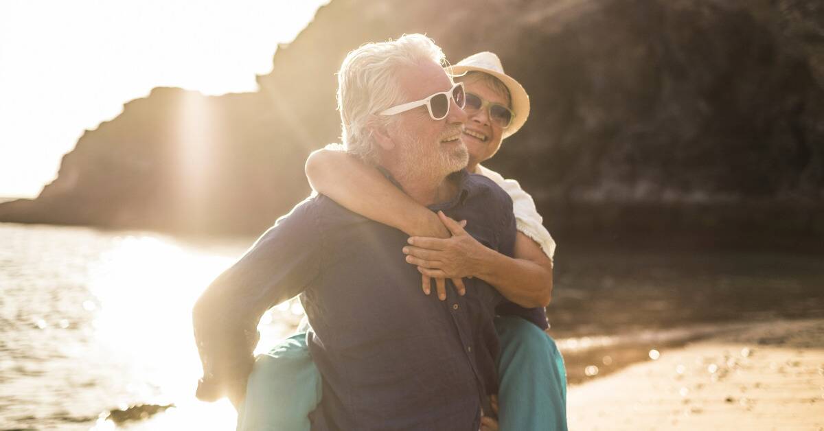 A couple on a beach, the man giving the woman a piggyback ride.