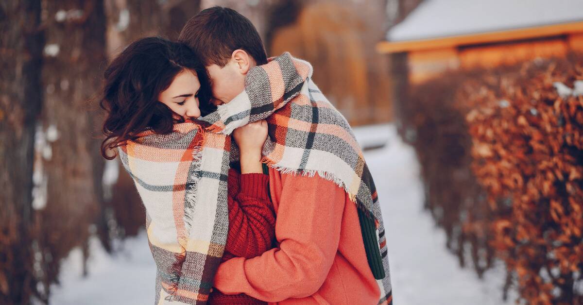 A couple hugging outside in the winter, a blanket wrapped around them.
