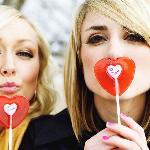 Two sisters both holding up heart-shaped valentine's day lolipops.
