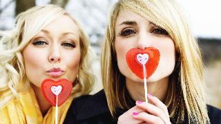 Two sisters both holding up heart-shaped valentine's day lolipops.